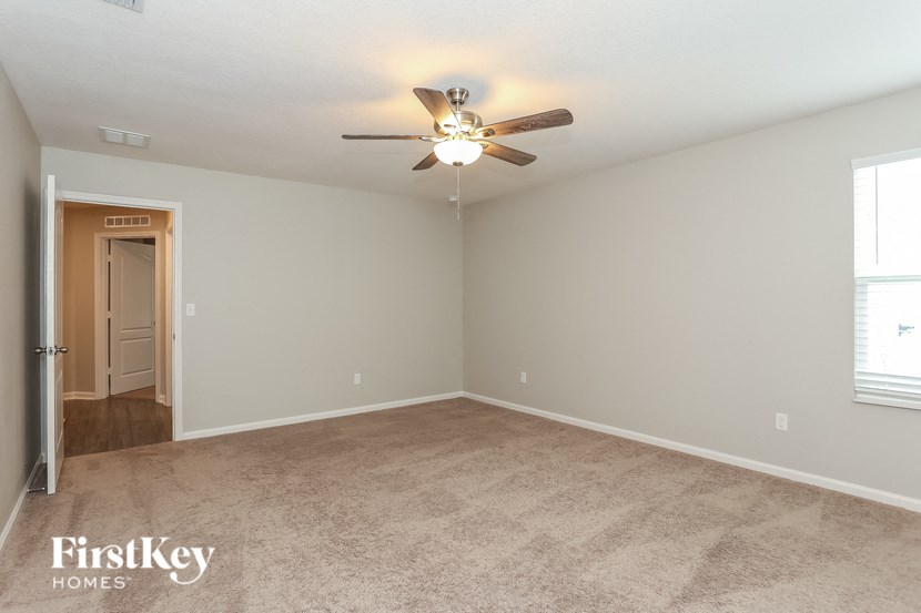 an empty living room with a ceiling fan and a door to a hallway