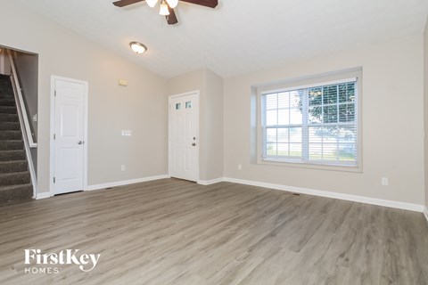 A spacious room with a staircase on the left and a window on the right.