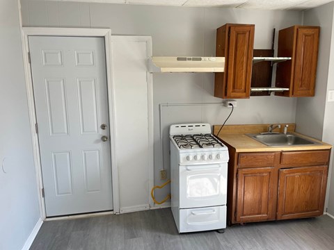 A white door is open in a kitchen with a white stove and wooden cabinets.