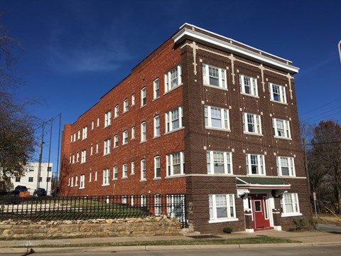 A red brick building with a green roof and a black fence in front.
