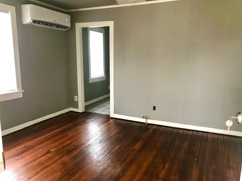 A room with wooden flooring and a door leading to a hallway.