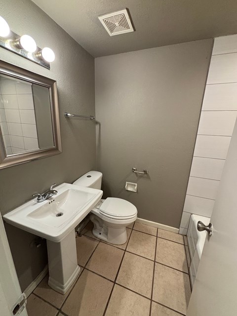 A bathroom with a toilet, sink, and mirror.