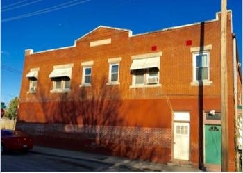 A red brick building with a green door and a tree in front.
