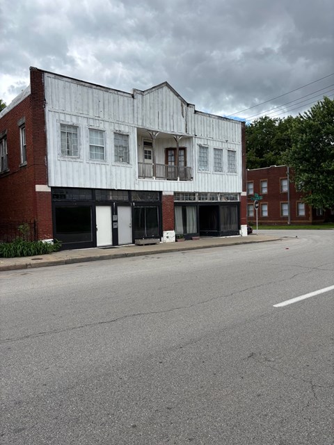 A white building with a balcony is on the corner of a street.