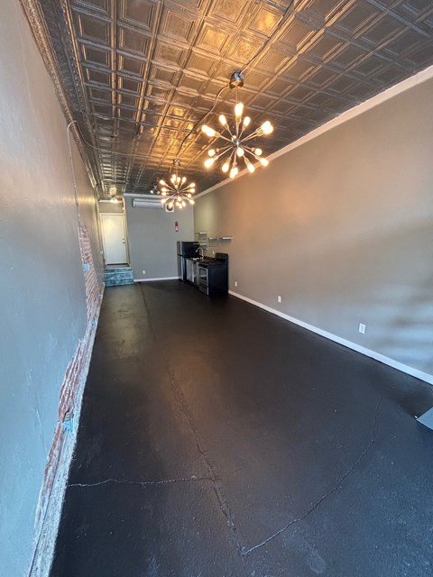 A long, empty room with a chandelier hanging from the ceiling.