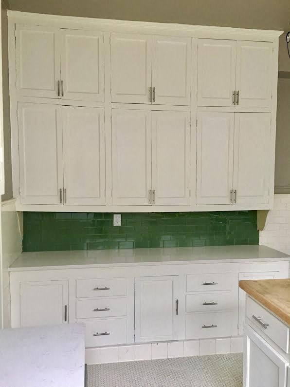 a white kitchen with white cabinets and a green wall