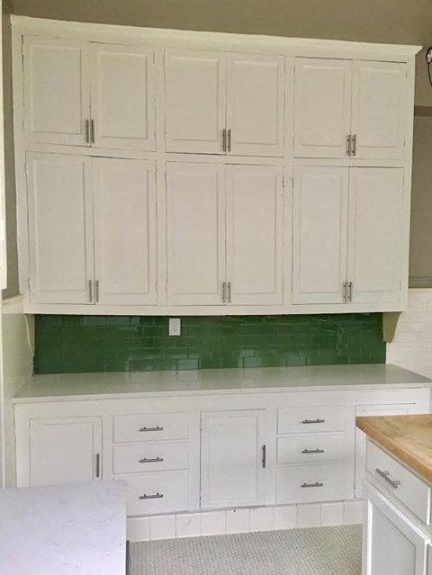 a white kitchen with white cabinets and a green wall