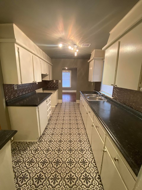 a kitchen with white cabinets and black counters and a tiled floor