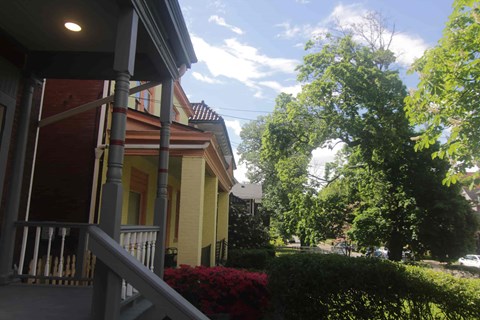 A yellow house with a porch and a tree in front.