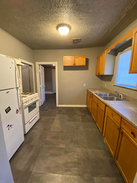 A kitchen with a white fridge, wooden cabinets, and a sink.