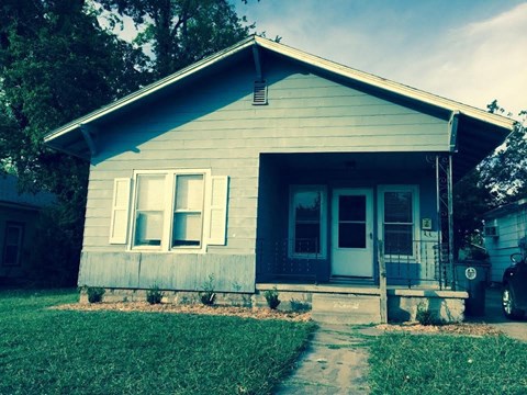 A small house with a porch and a trash can in front.