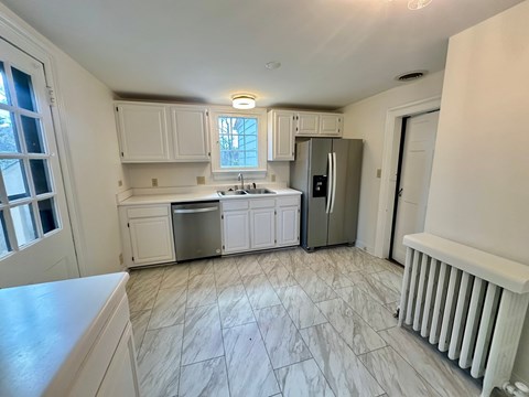 A kitchen with white cabinets and a marble floor.