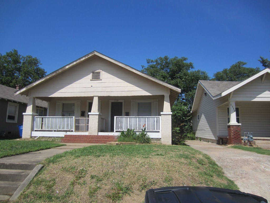 A house with a white porch and a black car in front.