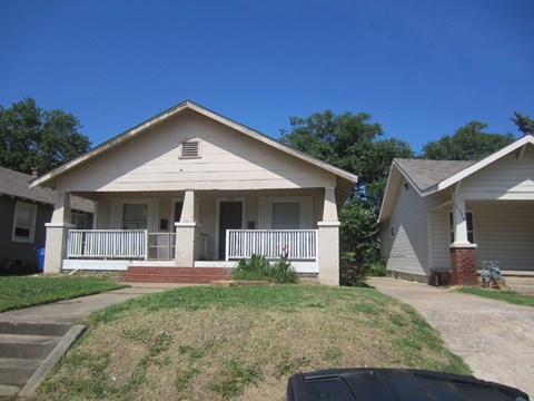 A house with a white porch and a black car in front.