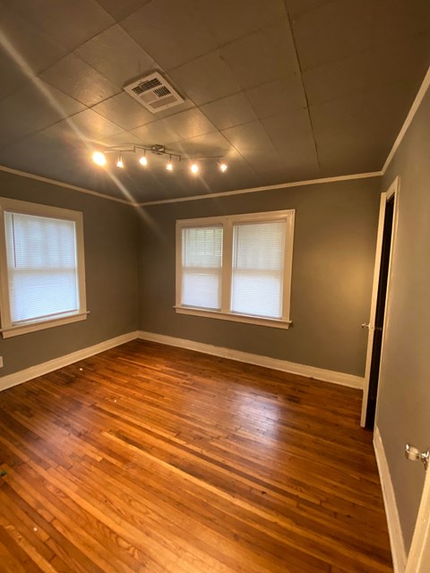 an empty room with wooden floors and two windows