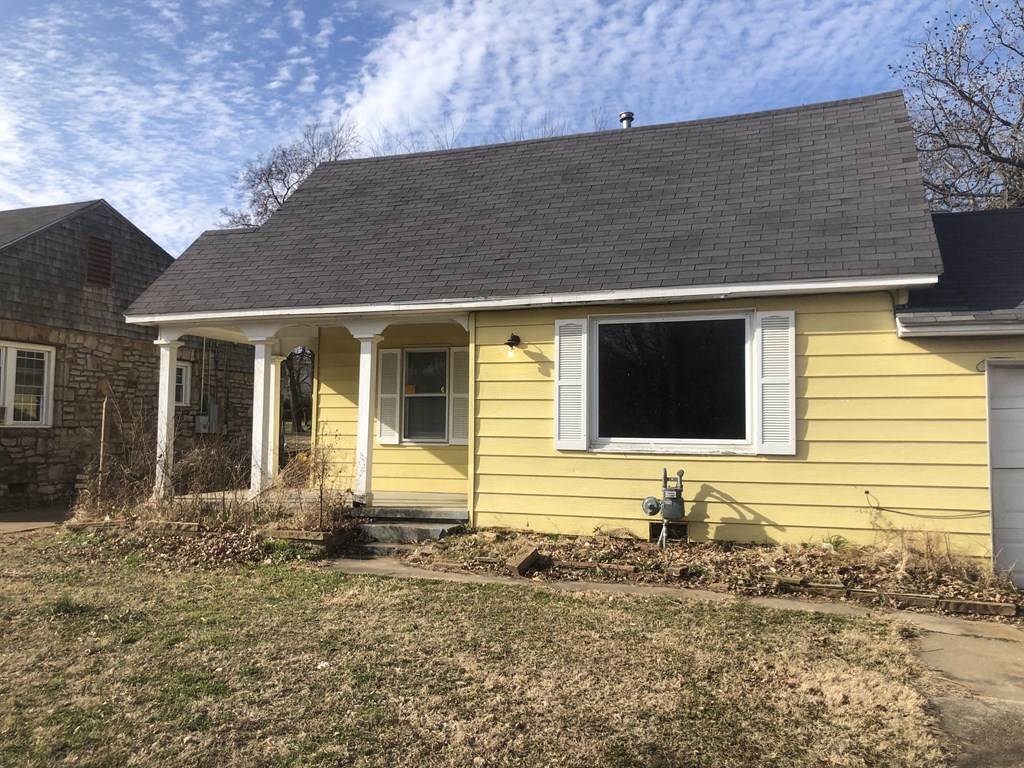 A yellow house with a grey roof and a window with white shutters.