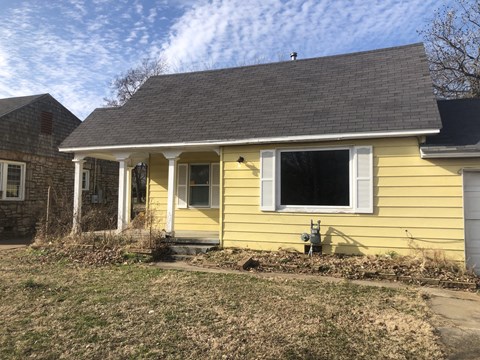 A yellow house with a grey roof and a window with white shutters.