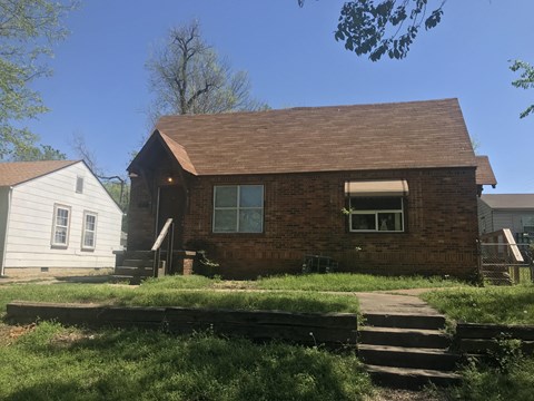 A small house with a brown roof and a white house in the background.