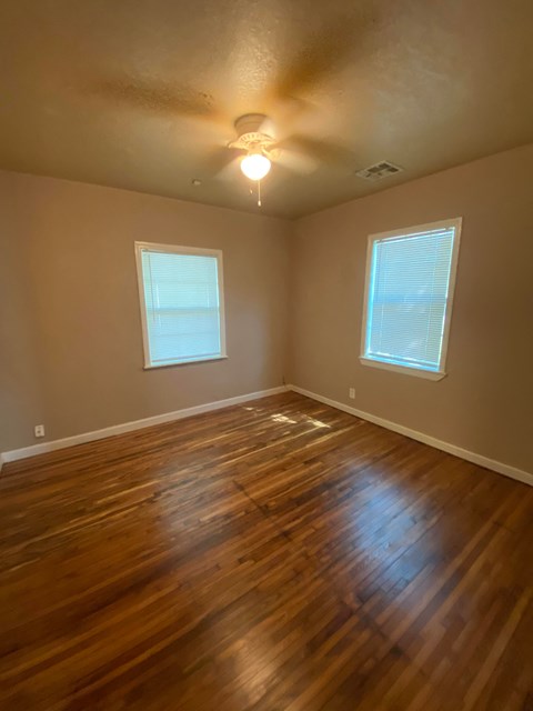 a empty room with a hard wood floor and two windows