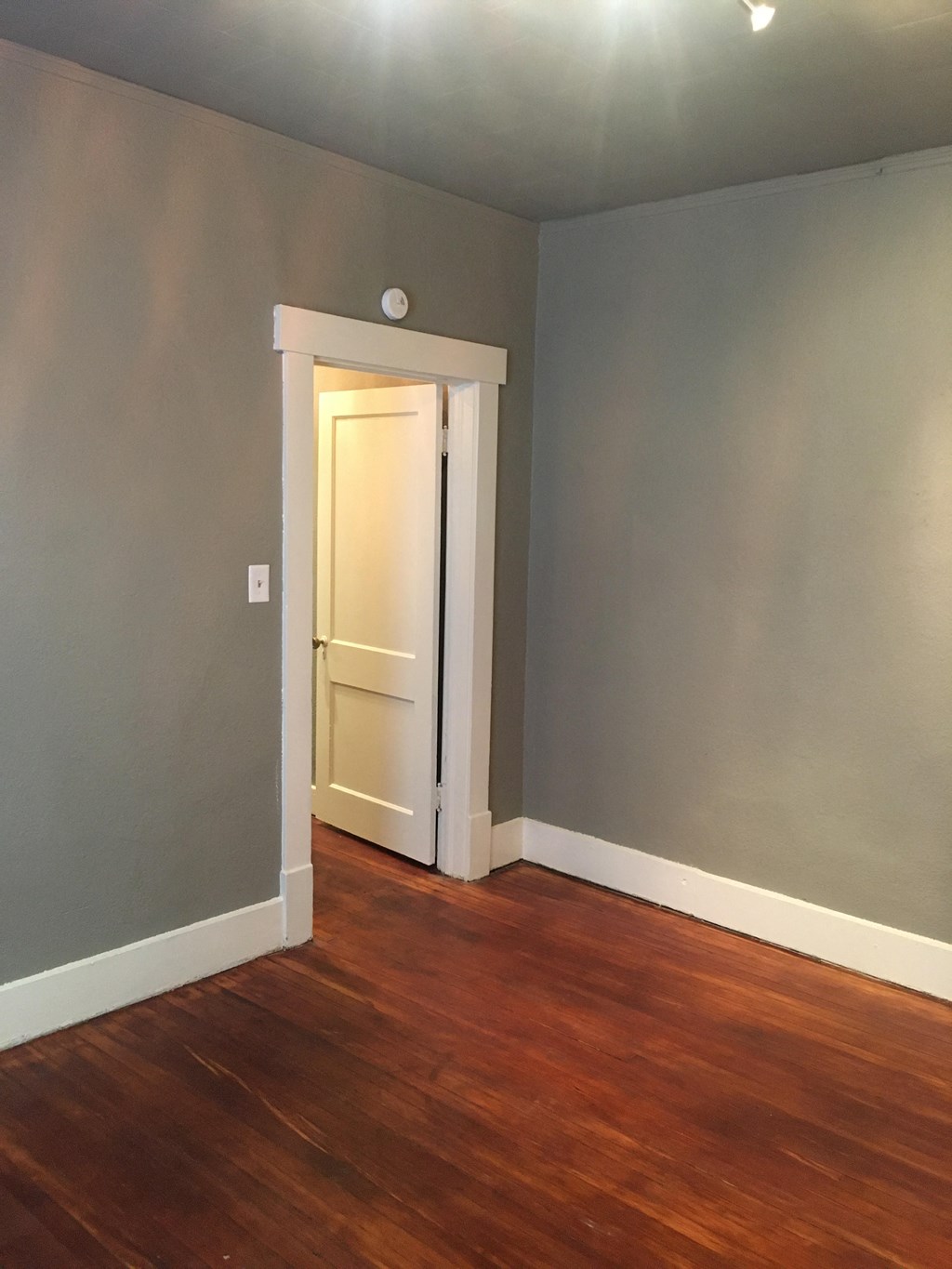 an empty room with wooden floors and grey walls and a white door