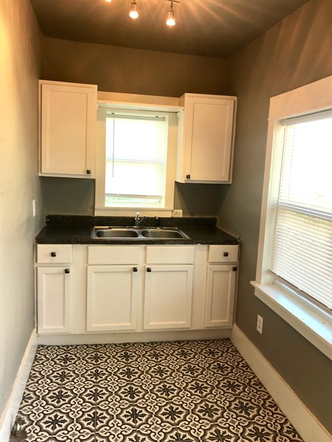 a small kitchen with white cabinets and a black and white tile floor