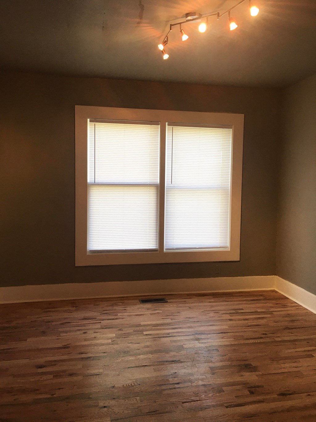 an empty living room with two windows and wood floors