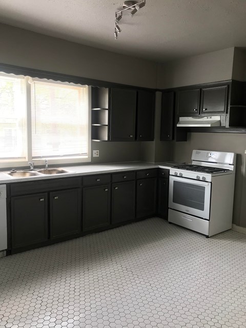 an empty kitchen with black cabinets and a stove and a window