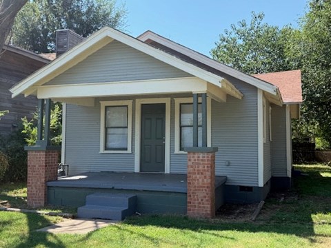 A small house with a grey siding and a brick pillar.