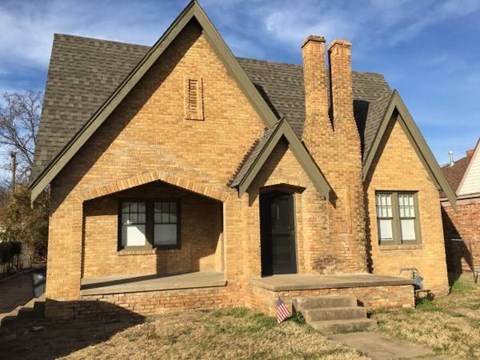 A small brick house with a black door and a small porch.