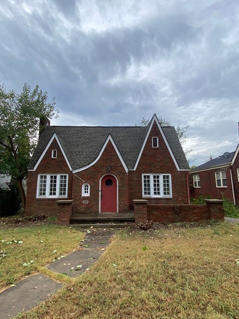 a brick house with a red door and a cloudy sky