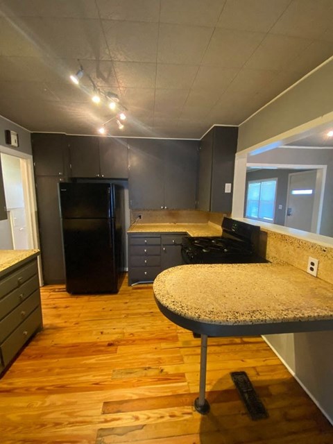 A kitchen with a black fridge and wooden floors.