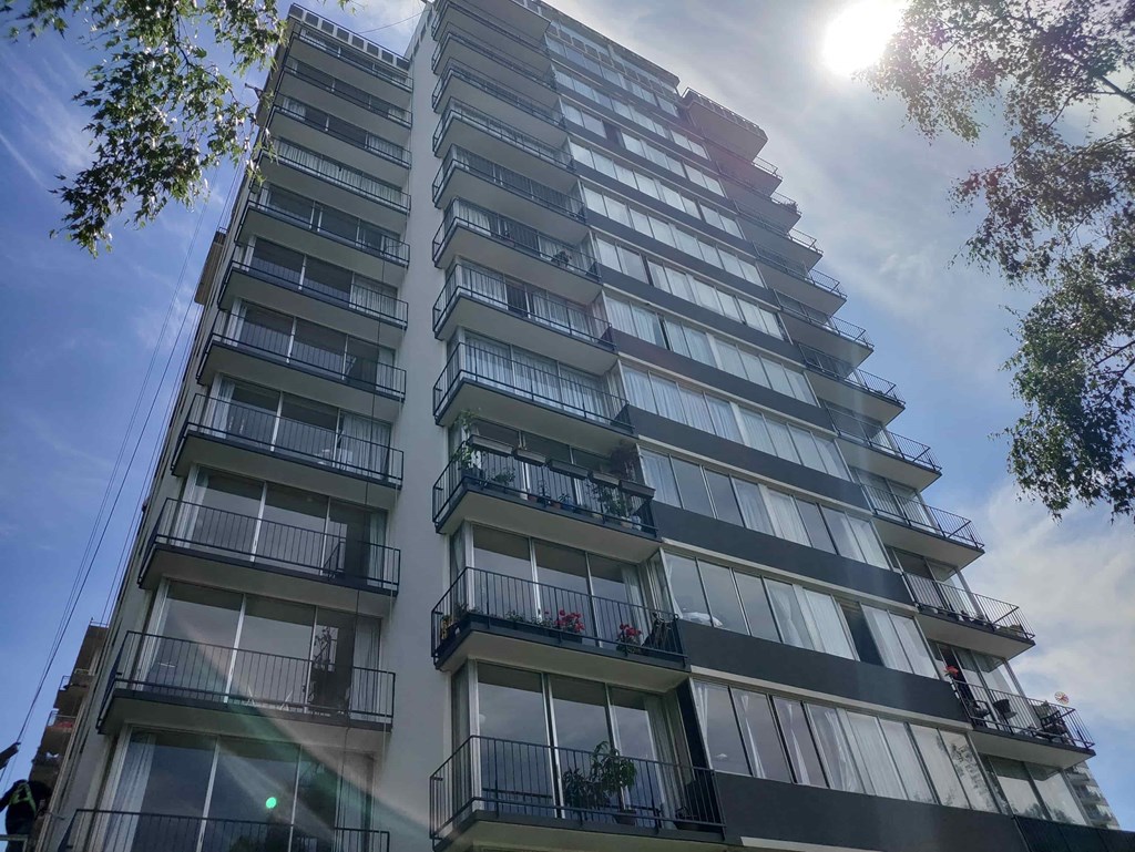 A tall building with balconies and windows is surrounded by trees.