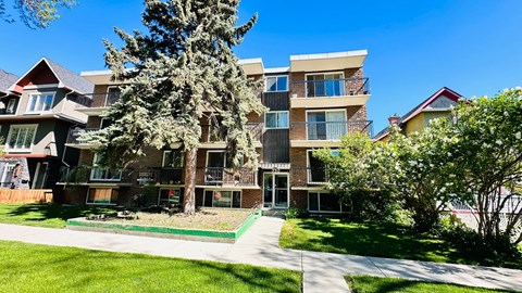 an apartment building with a sidewalk and trees in front of it