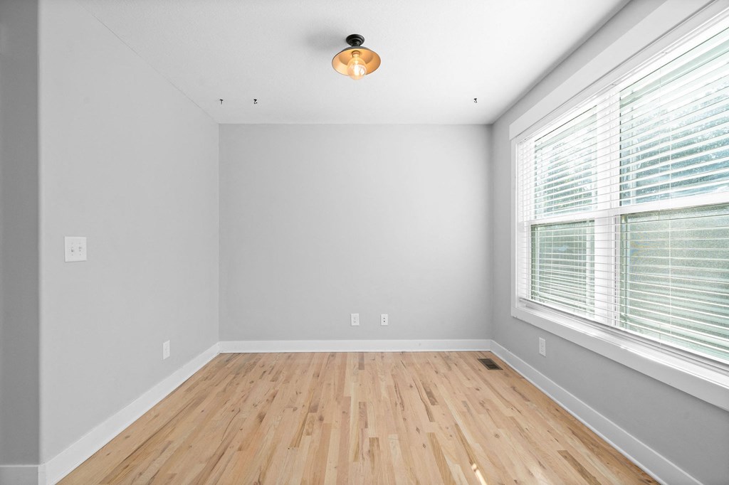 an empty room with two large windows and wood floors