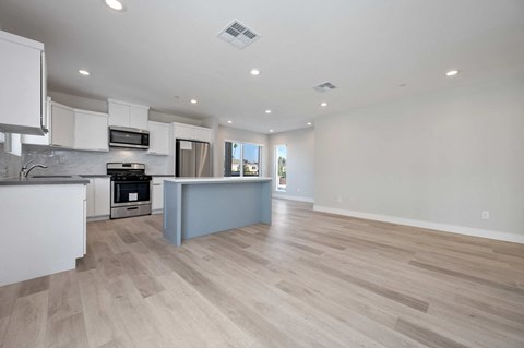 an open kitchen and living room with white walls and wood floors