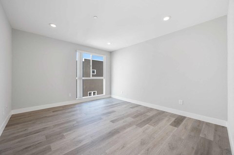a living room with white walls and a window and wood floors