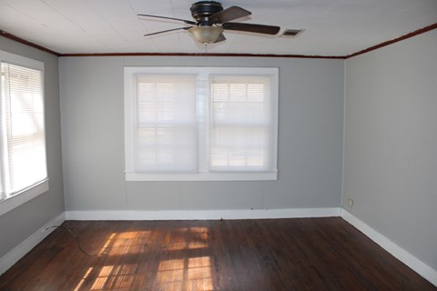 an empty room with a ceiling fan and two windows