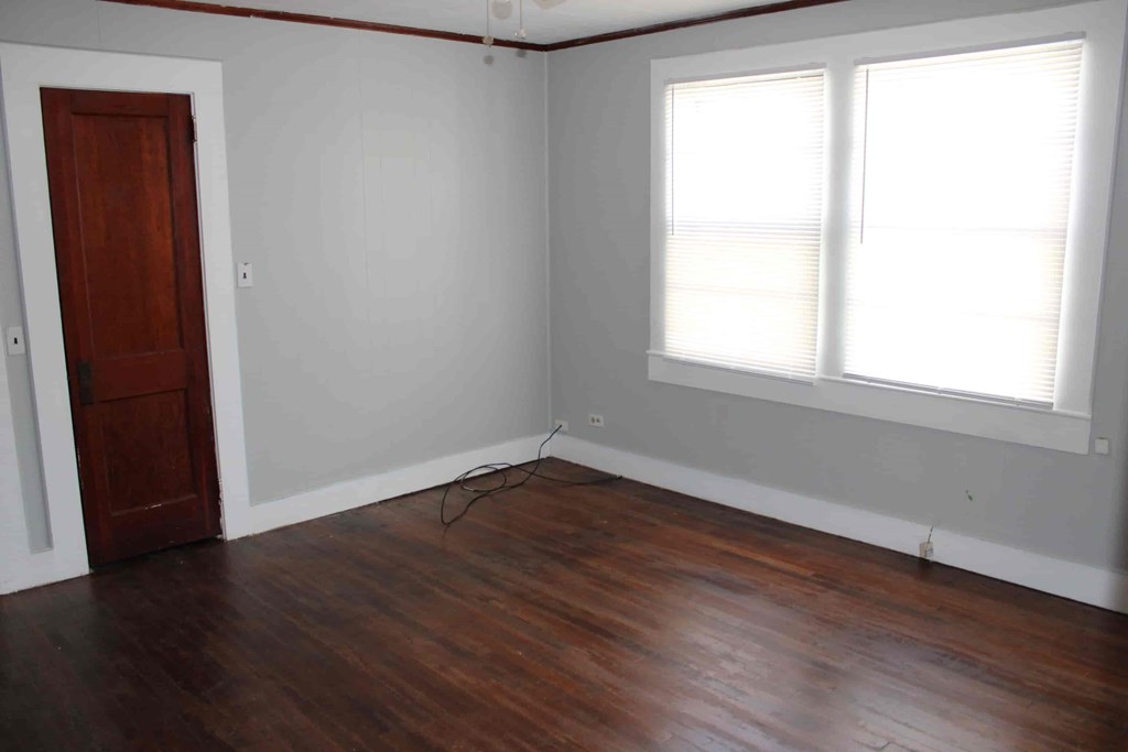 an empty room with wooden floors and a door and two windows