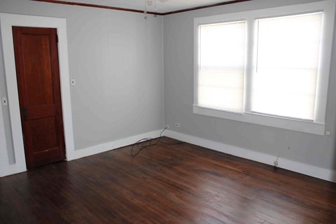 an empty room with wooden floors and a door and two windows