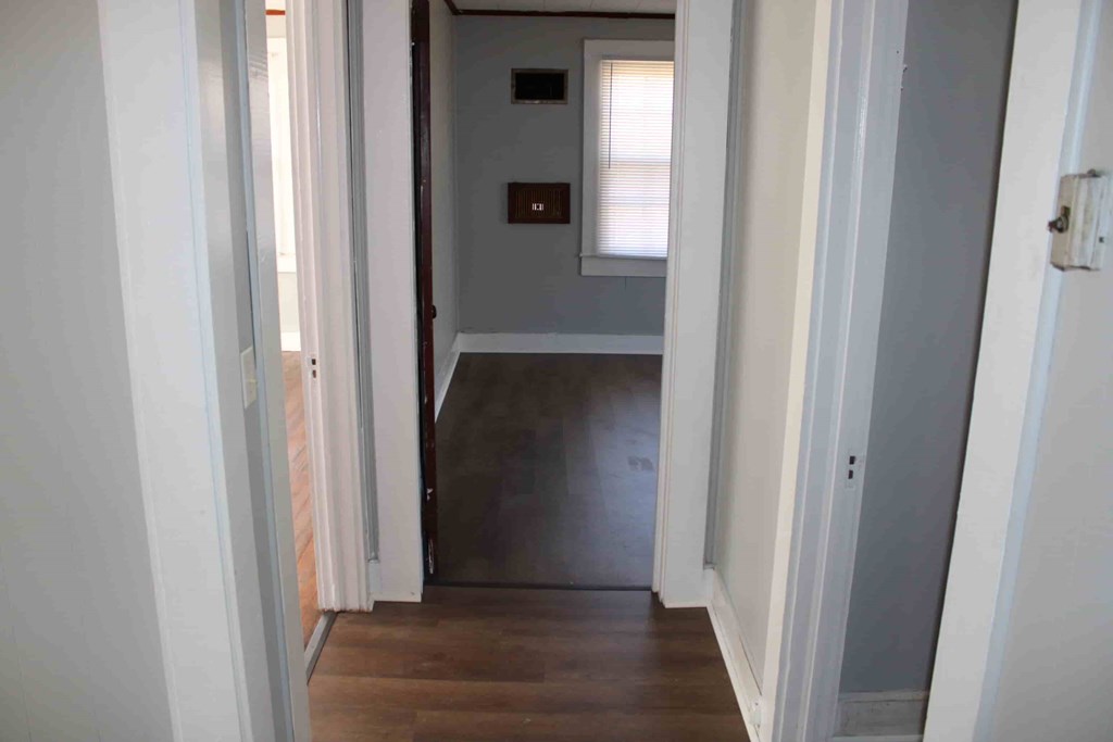a hallway with a door to a room with a hard wood floor and a window