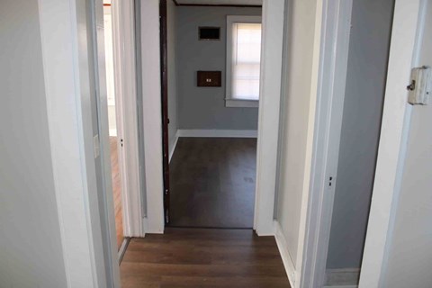 a hallway with a door to a room with a hard wood floor and a window