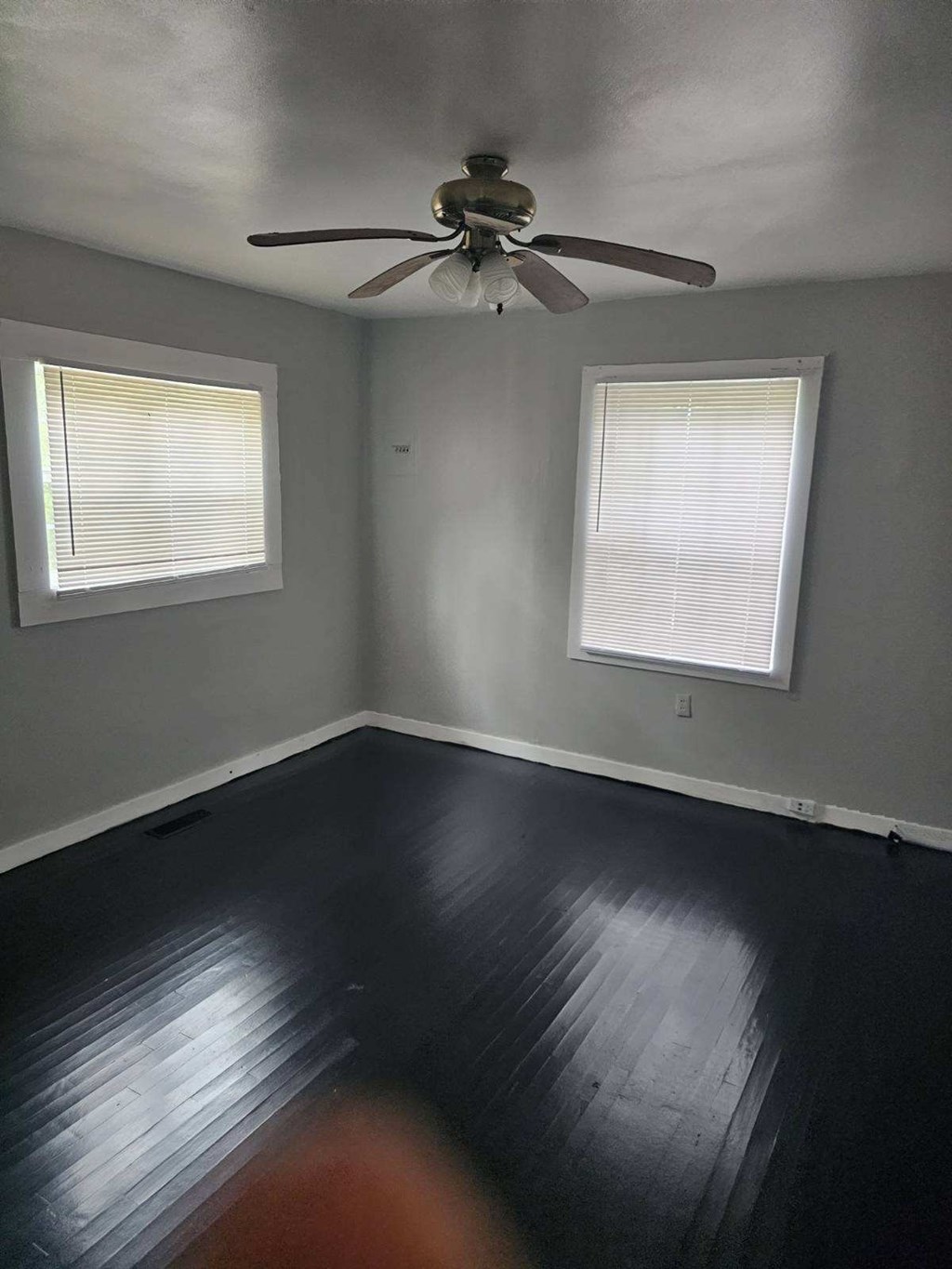 an empty room with a ceiling fan and two windows