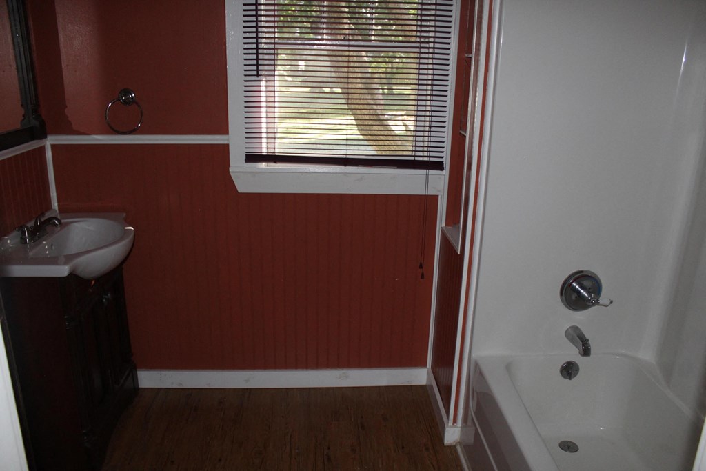 A red wall with a white sink and a white bathtub.