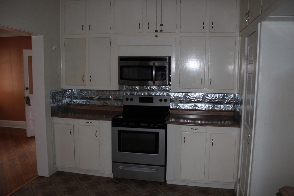 A kitchen with white cabinets and a stove top oven.