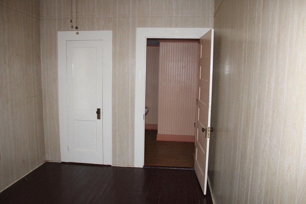 A room with a white door and a doorway leading to another room.