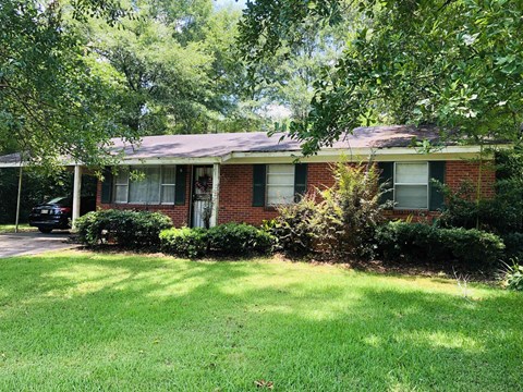 A house with a green lawn and trees in the background.