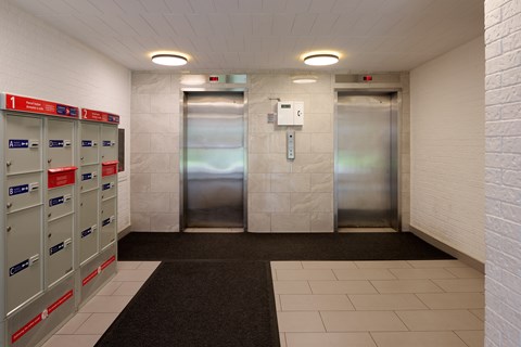 A hallway with a row of mailboxes on the left and two elevators in the middle.