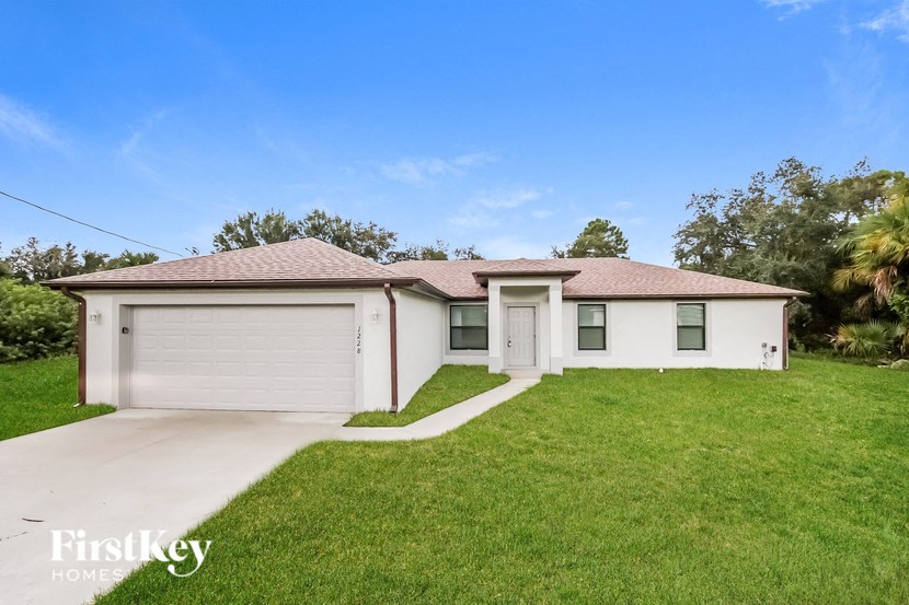 A white house with a brown roof and a garage door is for sale.