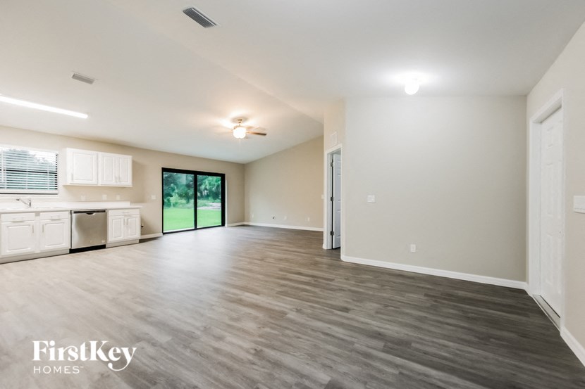 A spacious room with wooden flooring and a sliding glass door leading to a green outdoor area.