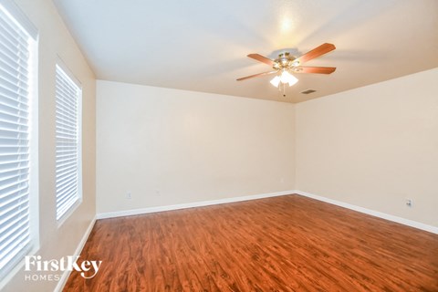 the living room of an empty home with wood flooring and a ceiling fan